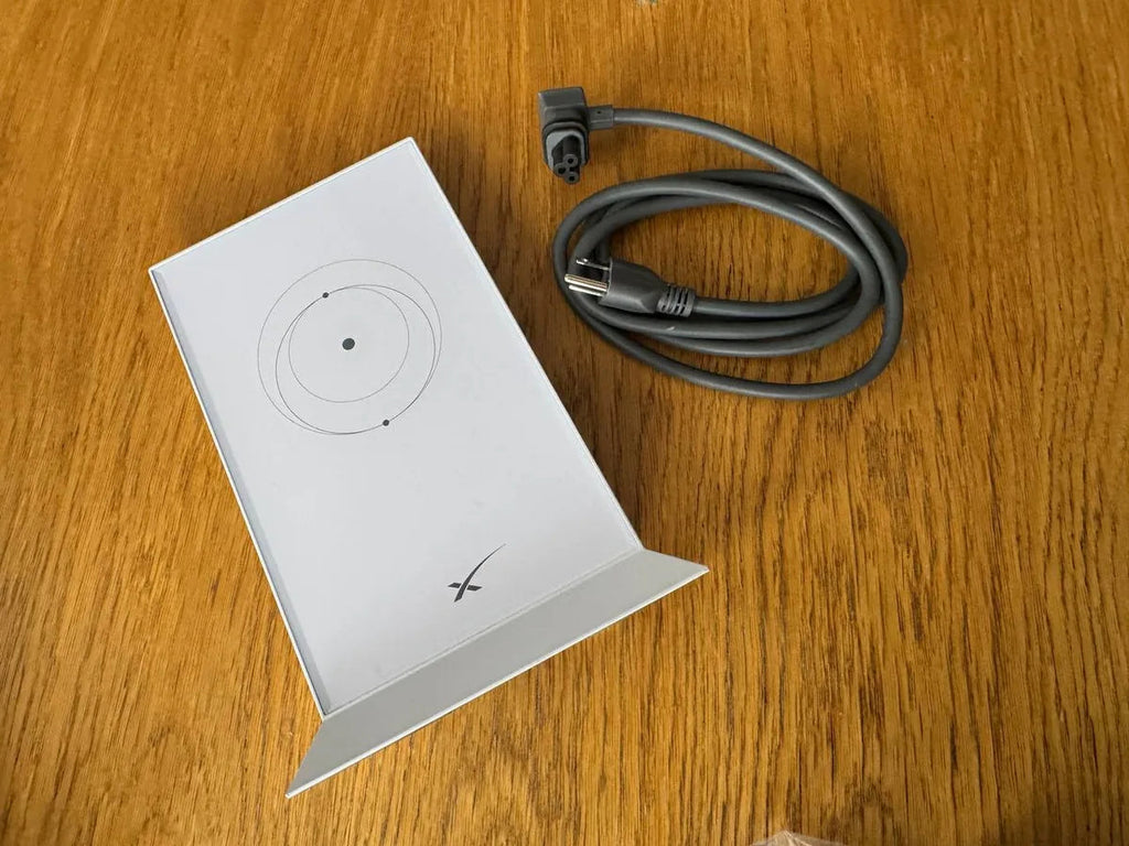 Overhead view of the Starlink Gen 2 router lying flat next to its coiled grey AC power cord.